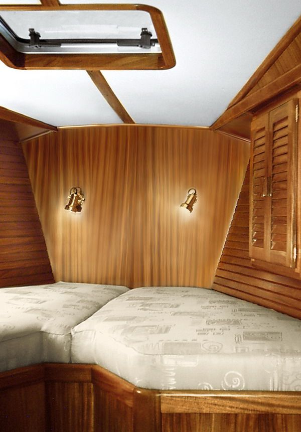 The forward cabin V-berth in solid mahogany, with brass reading lights and an overhead hatch.