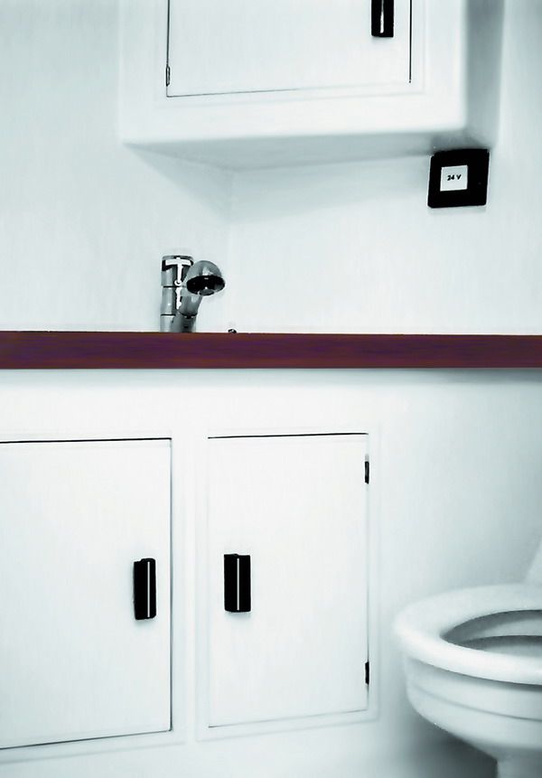 The heads compartment — white lockers with mahogany trim, a chrome mixer tap and a 24-volt outlet.