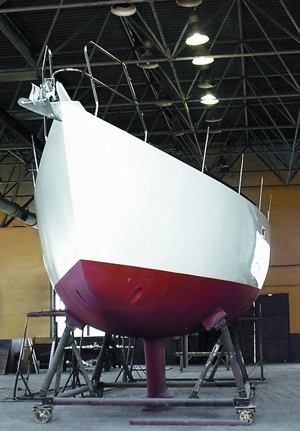Bow quarter view of the round-bilge steel hull on its cradle, showing the hull form and bow pulpit.