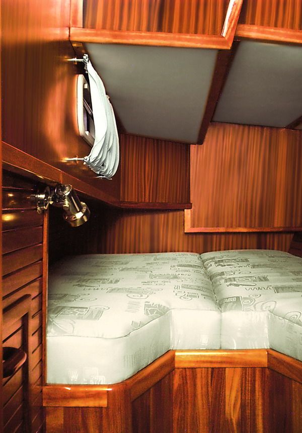 A double-berth cabin in solid mahogany with a brass reading light and an overhead hatch.