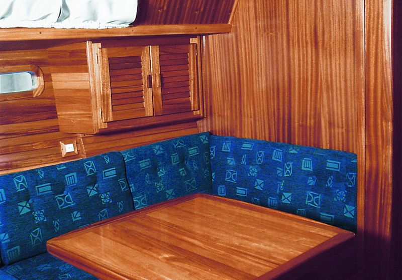 The saloon dinette — a U-shaped settee in blue upholstery around a solid mahogany table.