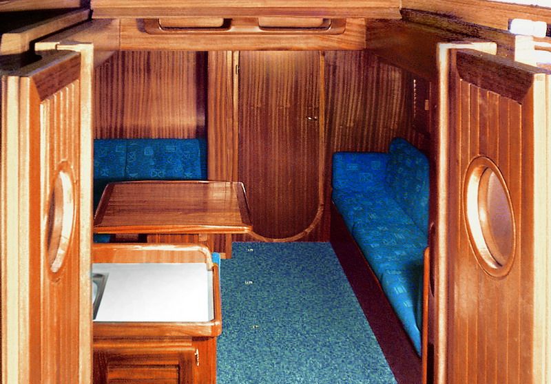 The main saloon looking forward, with solid mahogany joinery, blue settees and a drop-leaf table.